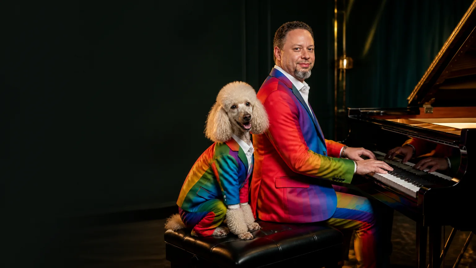 Tristan Desechenes playing a black grand piano beside a cream poodle, both wearing tailored rainbow suits in a luxurious studio